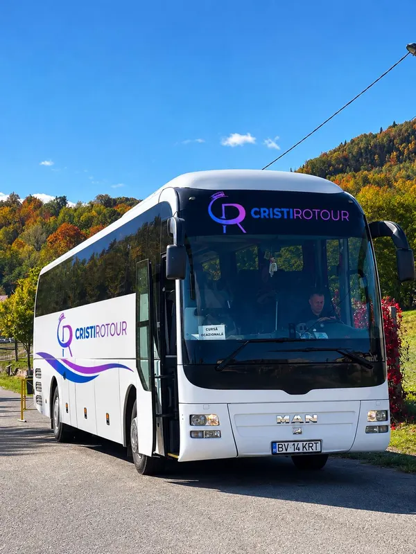 Autocar alb cu însemnele Cristi Rotour, parcat lângă o pădure de toamnă